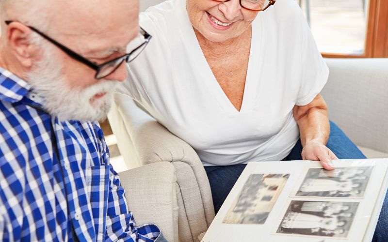 Photo of two old people looking at an album with old photos