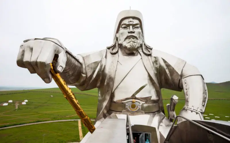 A large metallic statue of Genghis Khan riding a horse with grassy background