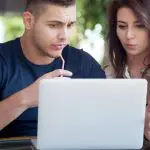 Photo of a man and a woman looking at the laptop in front of them looking confused