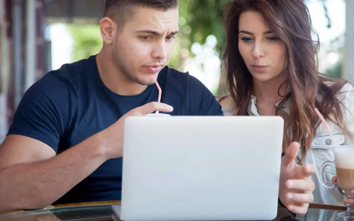 Photo of a man and a woman looking at the laptop in front of them looking confused