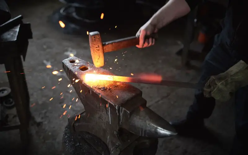 A photo showing what looks like a blacksmith with one hand holding a hammer hitting a heated iron.