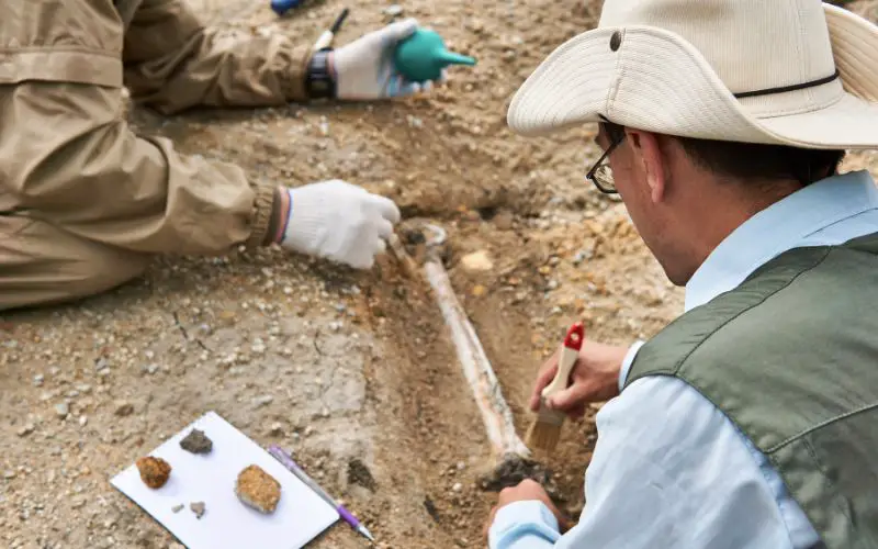 Two men cleaning what it looks like a bone in an archeology site